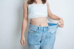 Young woman wearing oversized jeans to highlight a slimmer figure, representing weight loss success through diet, exercise, or liposuction treatment
