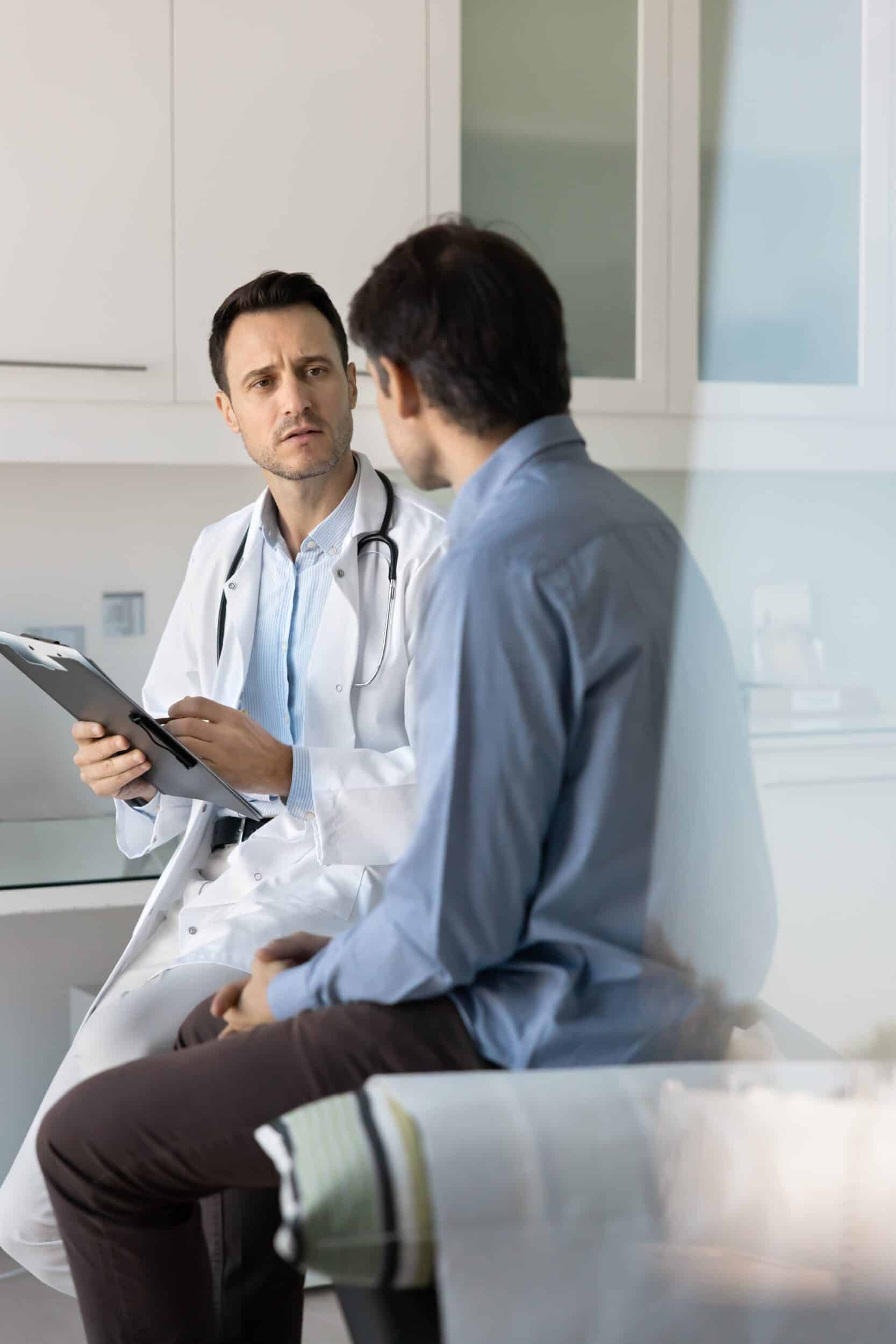 Concerned doctor examining a male patient and taking notes during a consultation about skin cancer treatment in a clinic