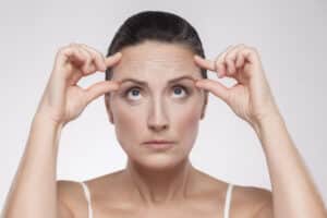 Middle-aged woman touching forehead and checking wrinkles, portrait concept of brow lift, anti-aging skincare, and facial rejuvenation.